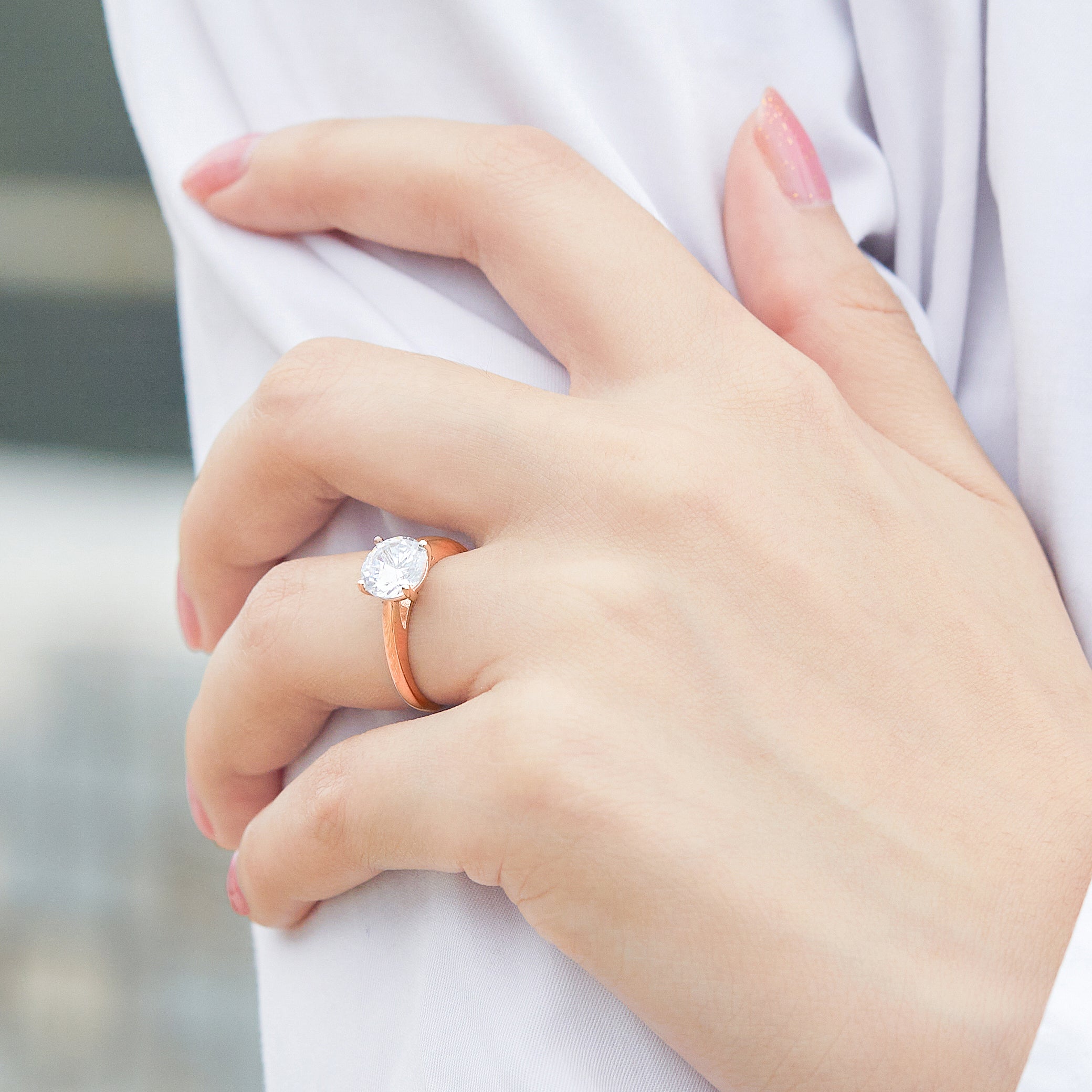 Close-up of a hand wearing a rose gold ring with a diamond on a blurred background