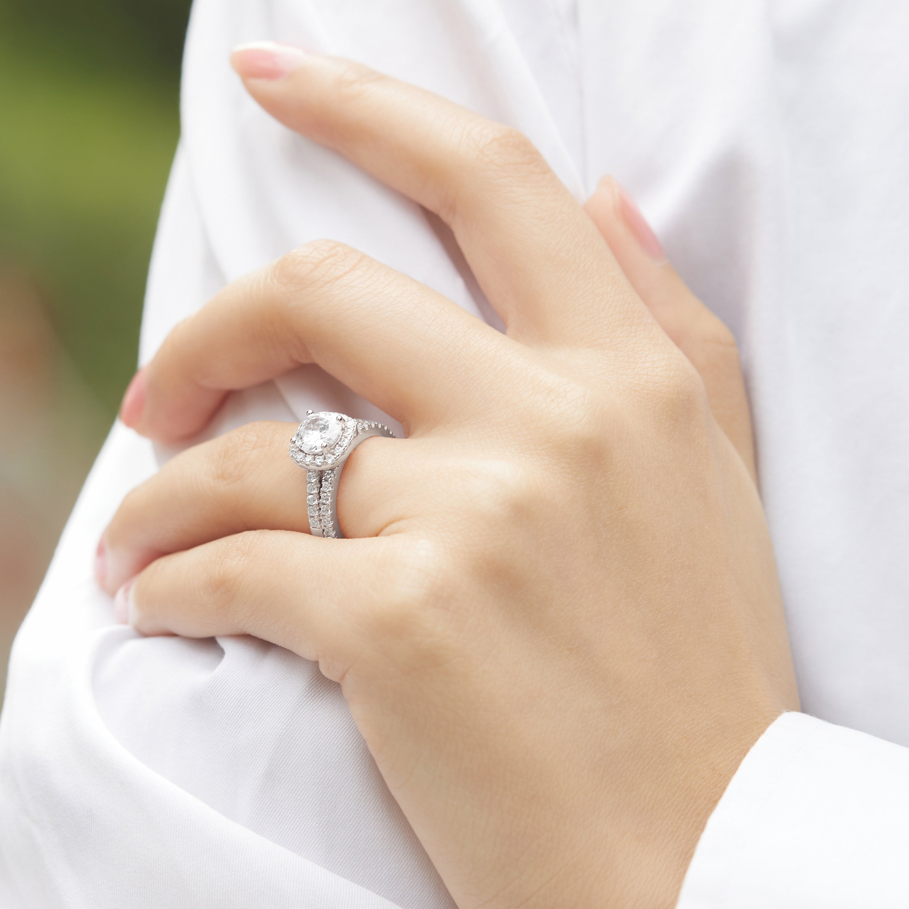 Close-up of a hand wearing a silver ring with a diamond on a blurred background