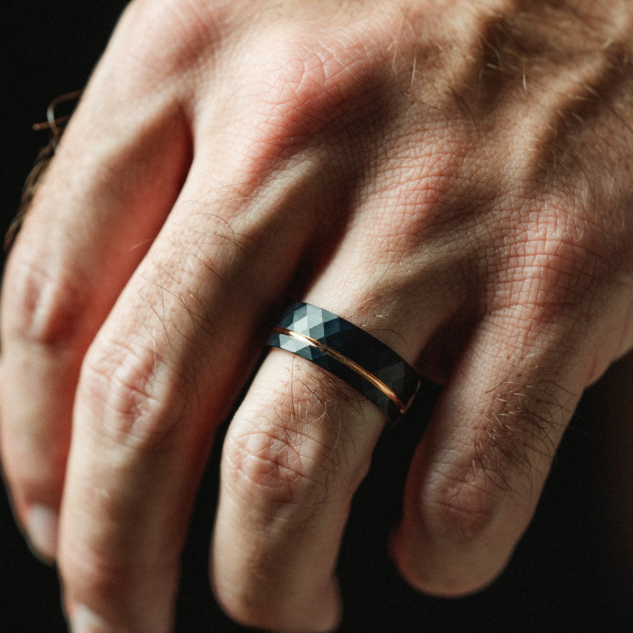 Hand wearing a black and gold ring against a dark background