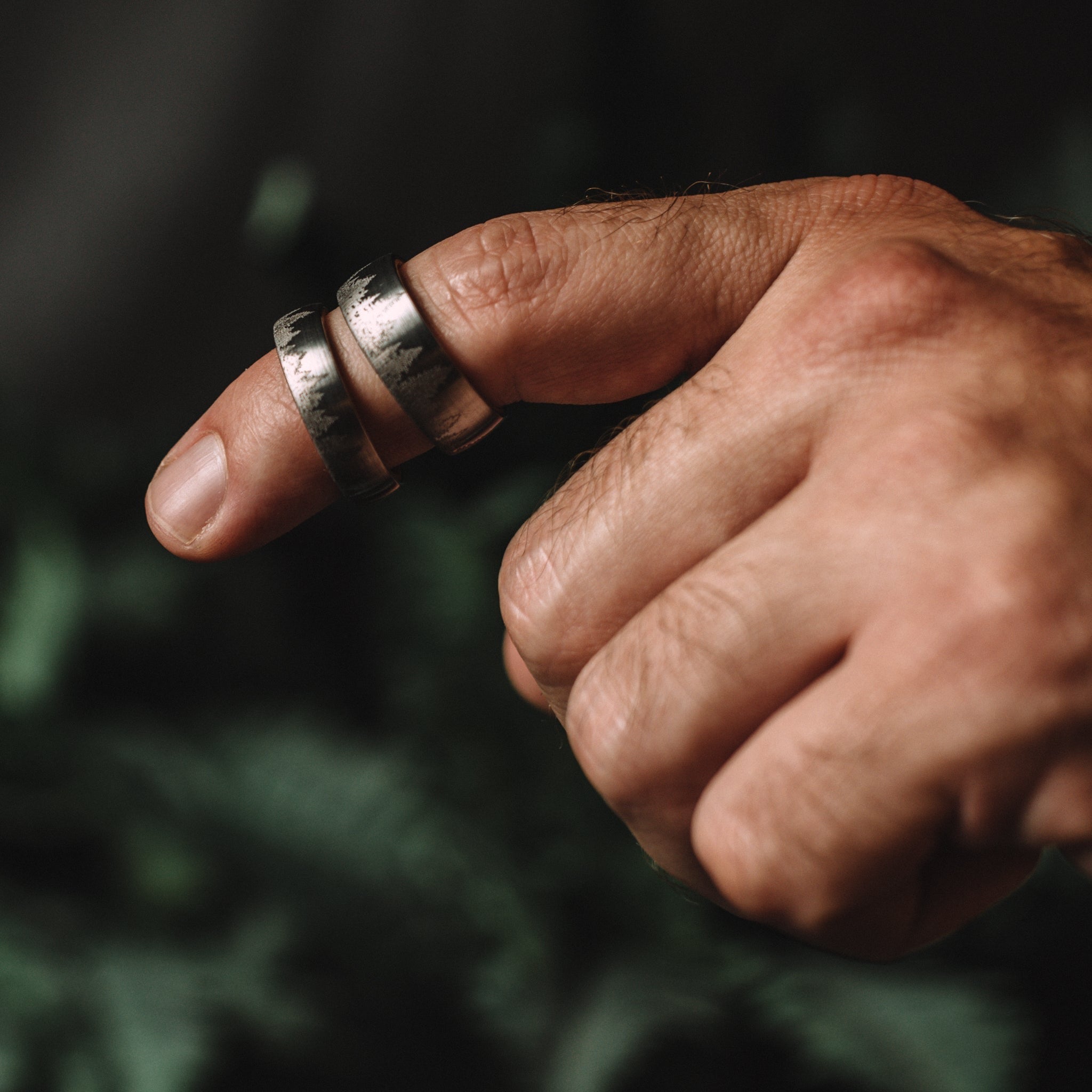 Close-up of a hand with two silver rings on a blurred green background