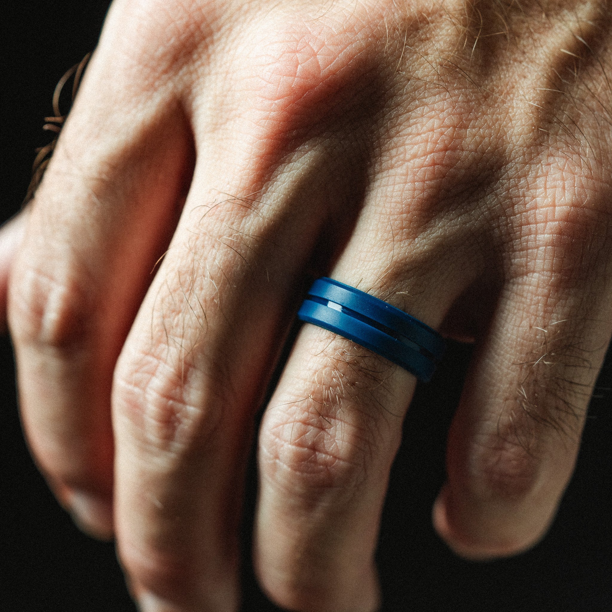 Hand wearing a blue ring on a dark background