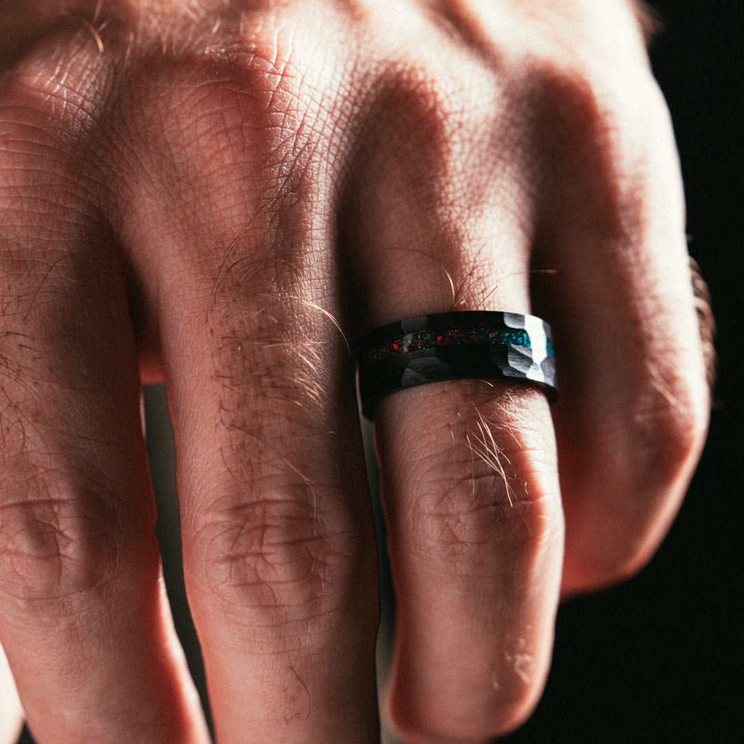 Close-up of a hand wearing a black ring with colorful stones on a dark background