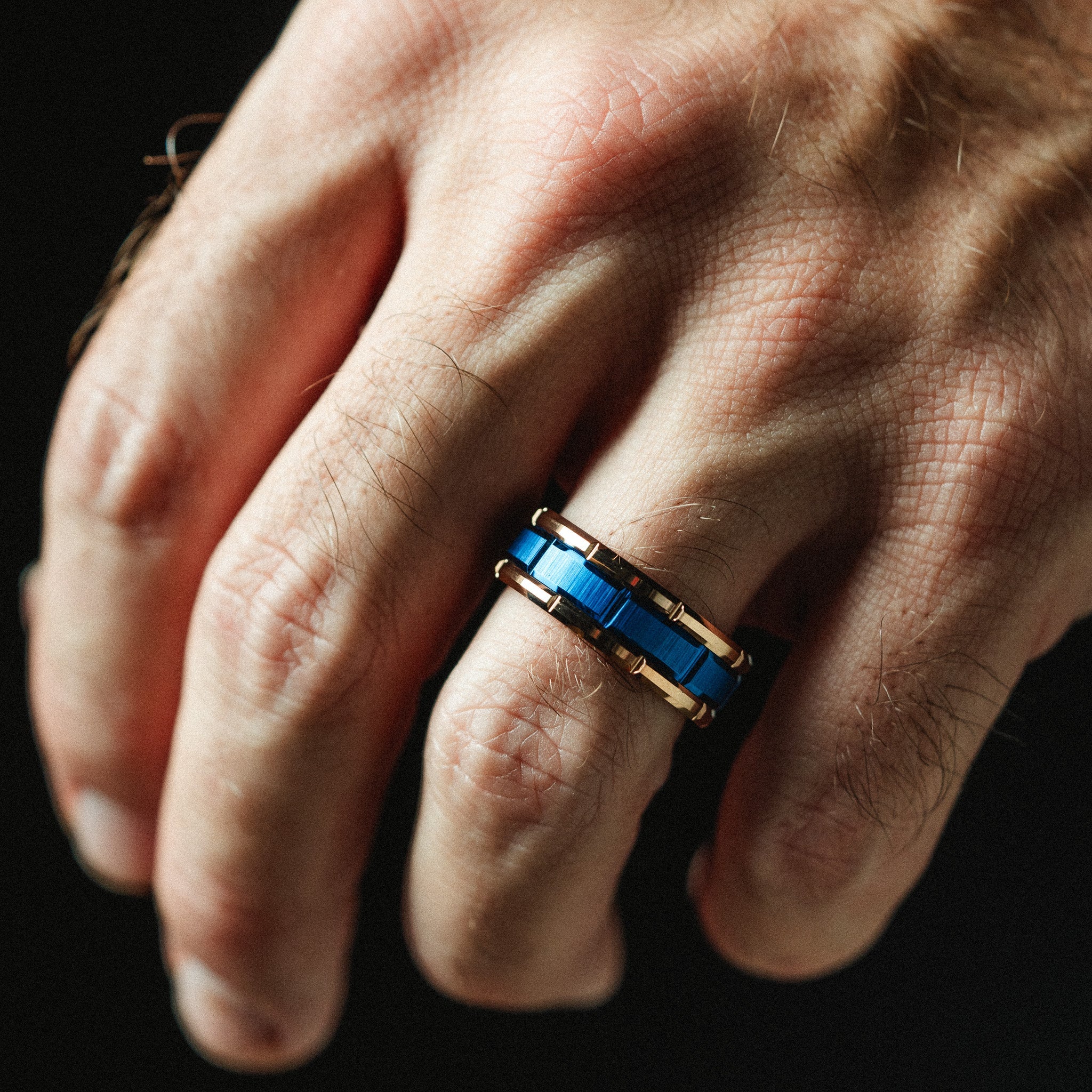 Hand wearing a blue and gold ring against a black background
