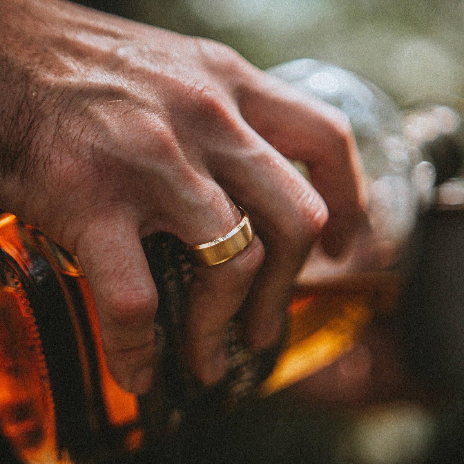 Hand holding a bottle of whiskey with a gold ring on a blurred background