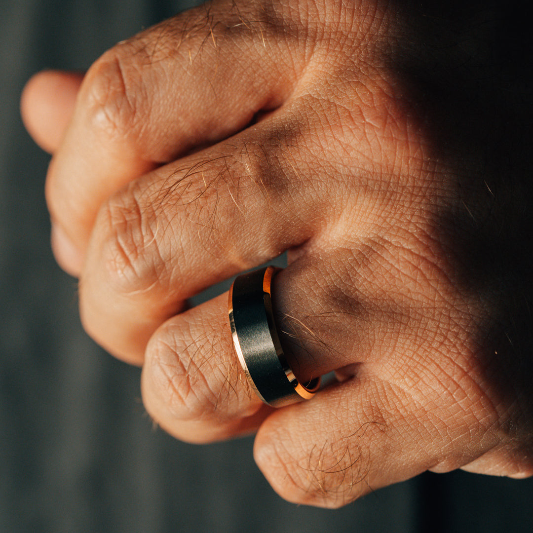 Close-up of a hand wearing a black ring with orange accents on a dark background