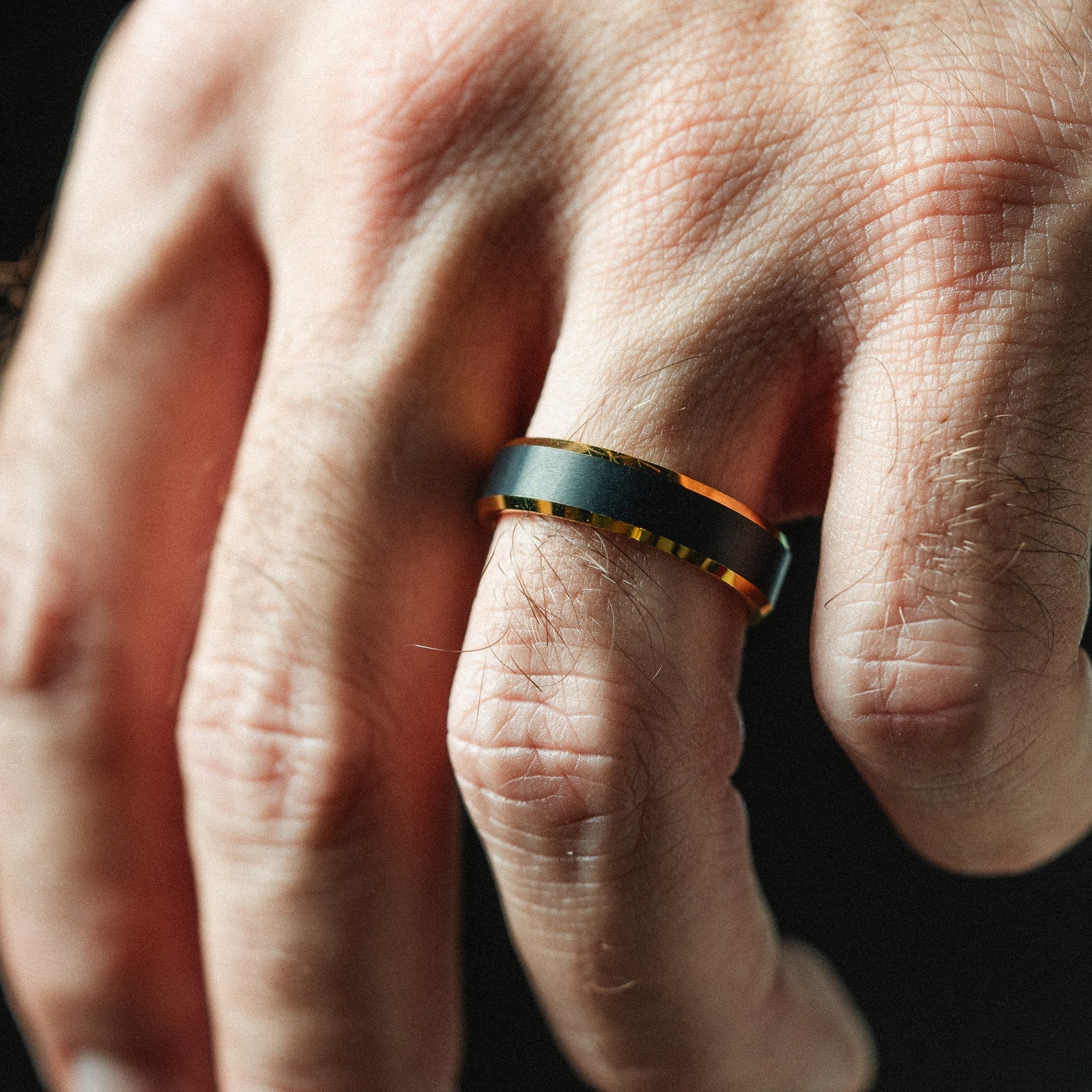 Close-up of a hand wearing a black and orange smart ring on a dark background