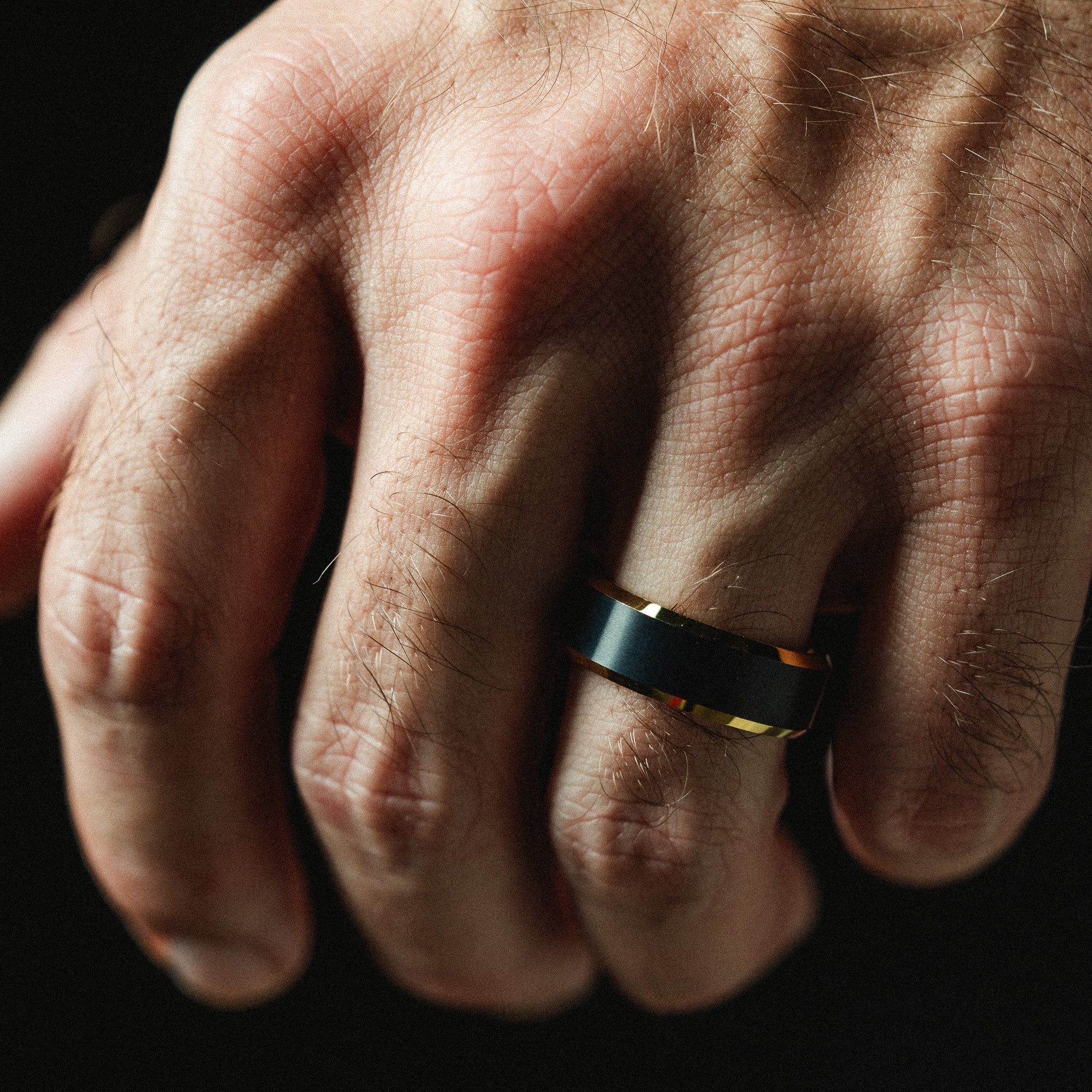 Close-up of a hand wearing a black ring with gold accents on a dark background