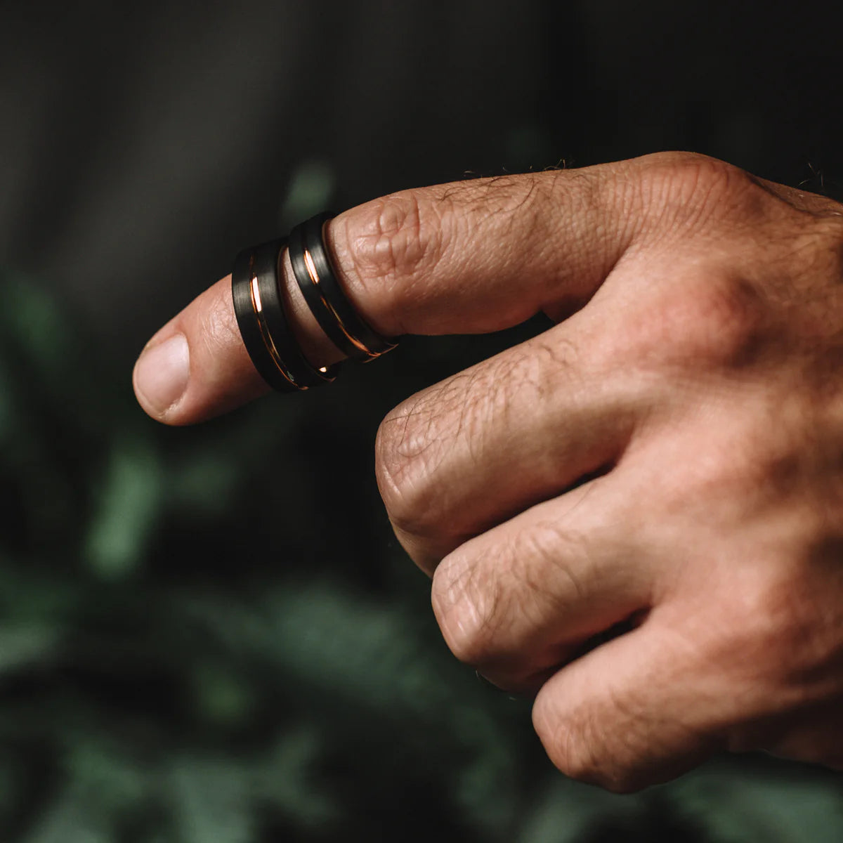 Hand wearing a black ring on a blurred green background