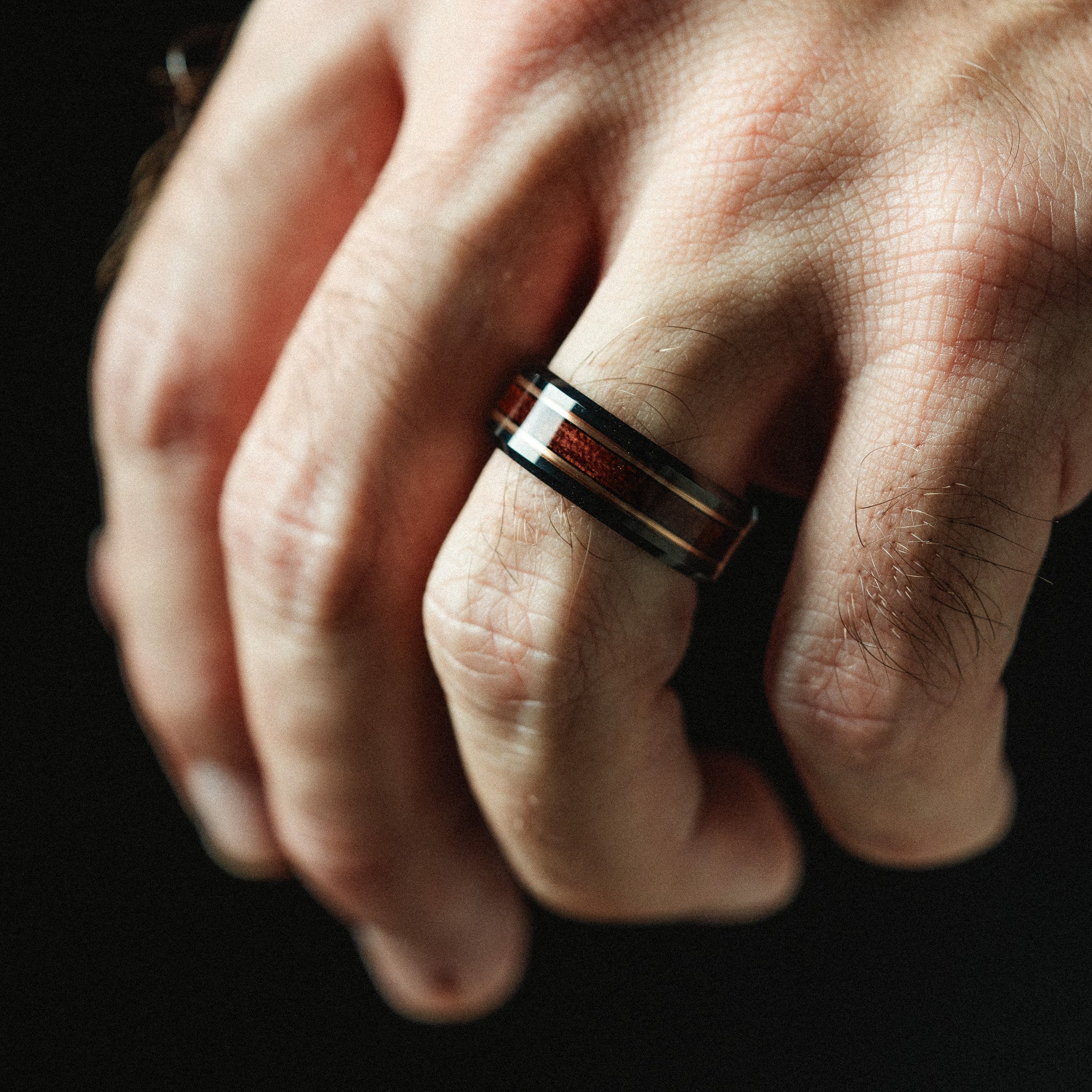 Close-up of a hand wearing a wooden ring on a dark background
