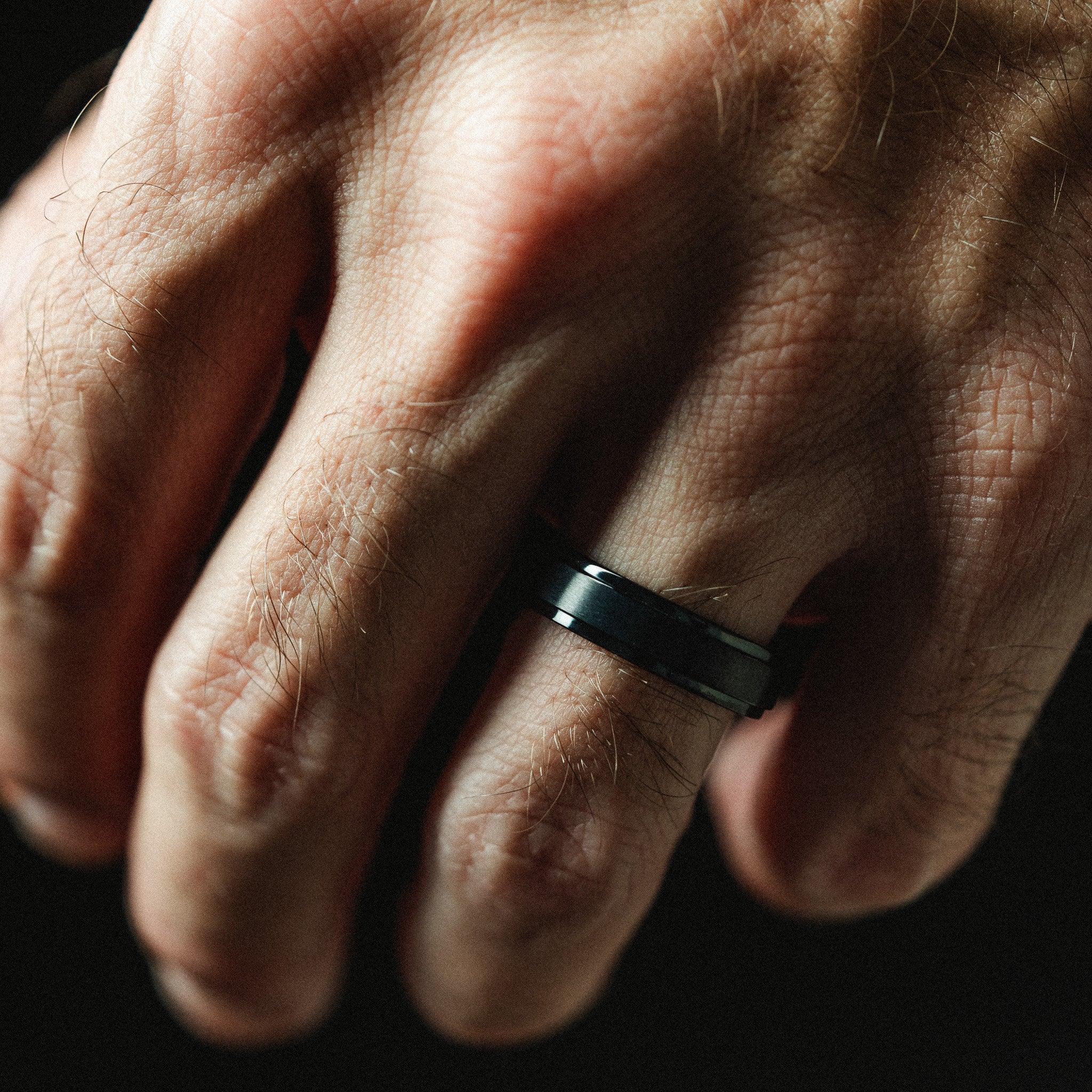Close-up of a hand wearing a black ring on a dark background