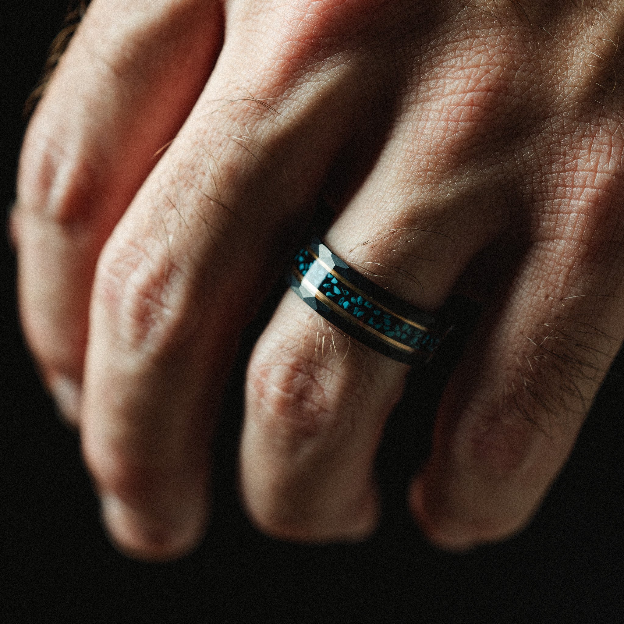 Close-up of a hand wearing a ring with blue stones on a dark background