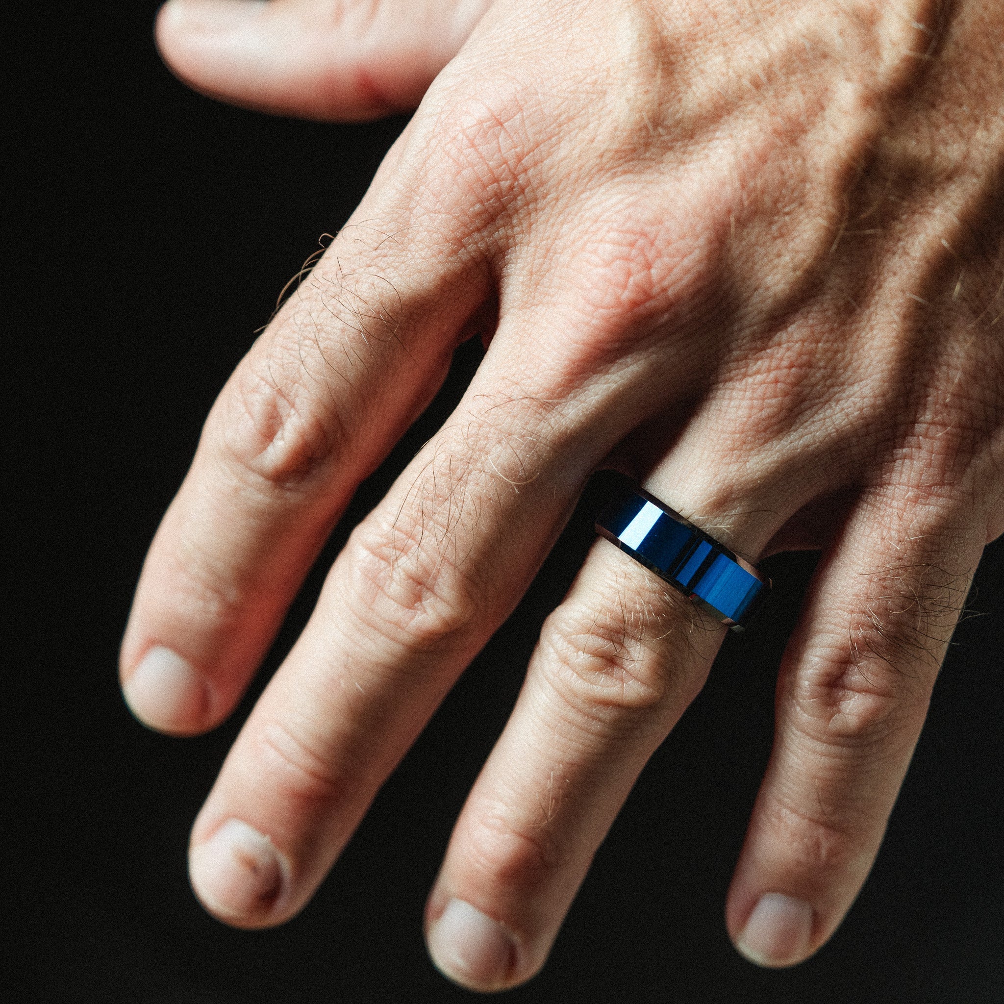 Hand wearing a blue ring on a black background