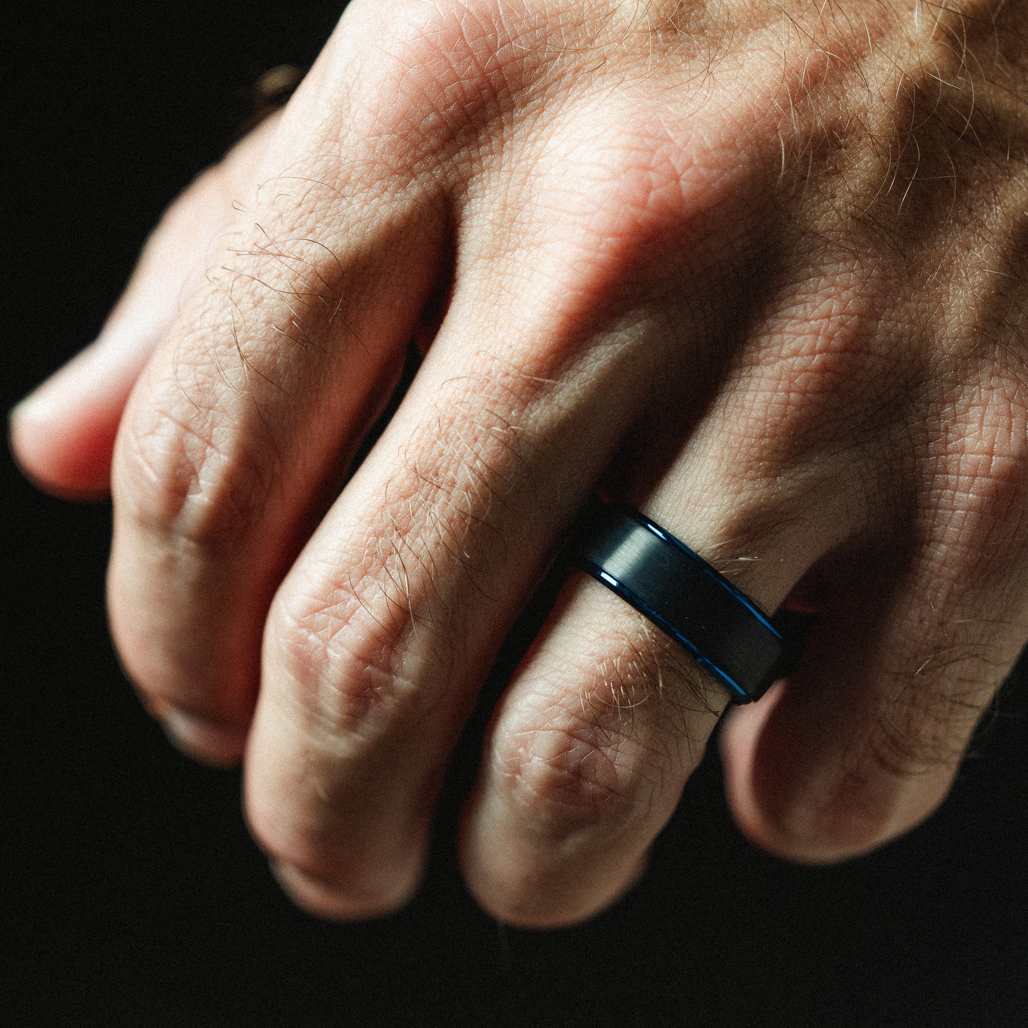 Close-up of a hand wearing a blue ring on a dark background