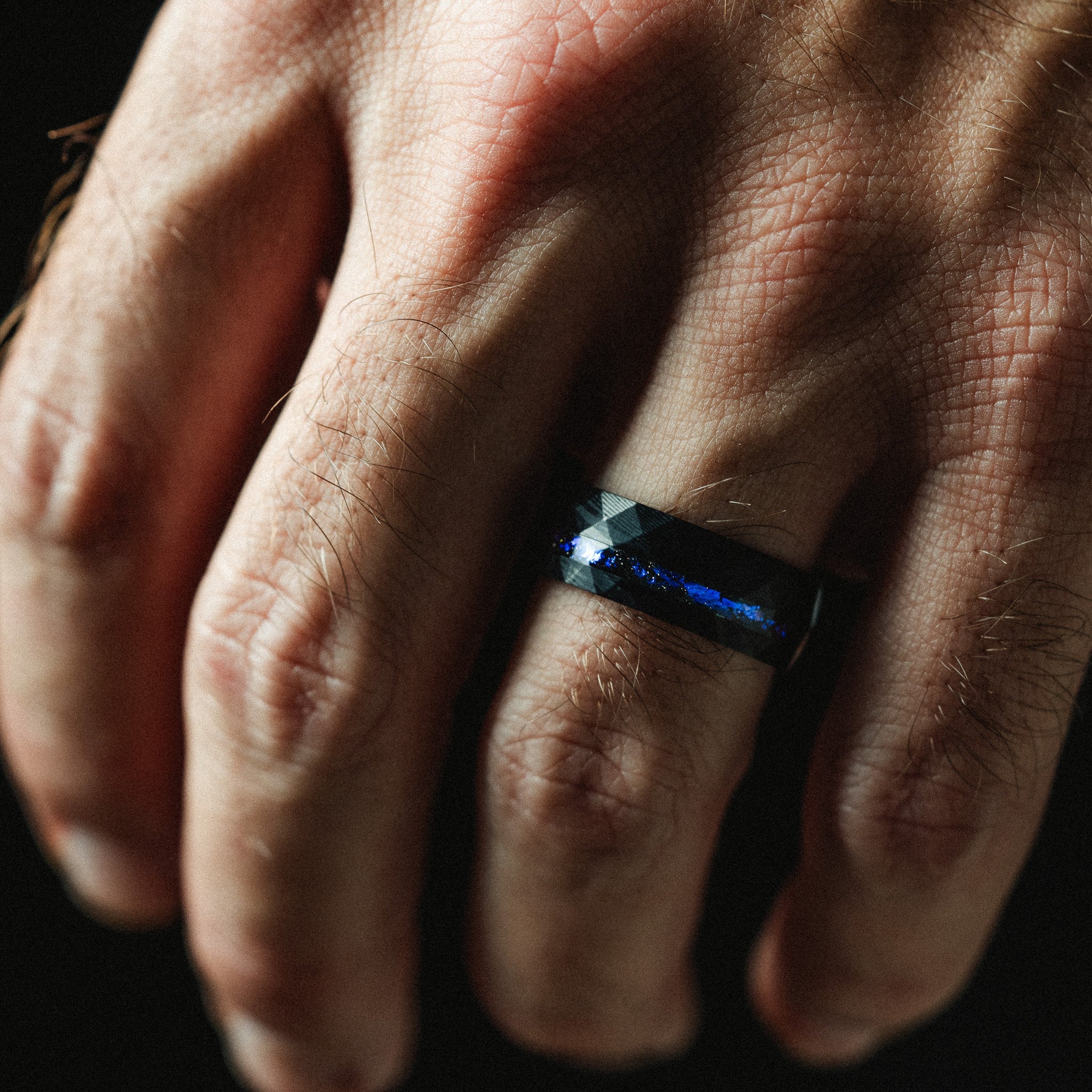 Close-up of a hand wearing a blue ring on a dark background