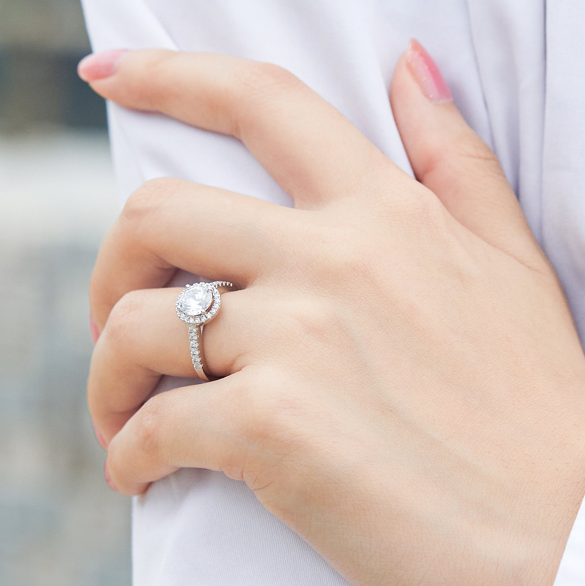 Close-up of a hand wearing a silver ring with a diamond on a blurred background