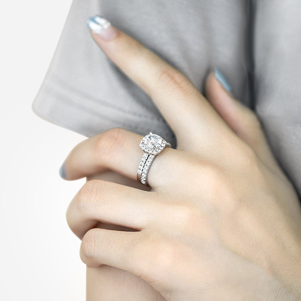 Close-up of a hand wearing a silver ring with a diamond on a neutral background