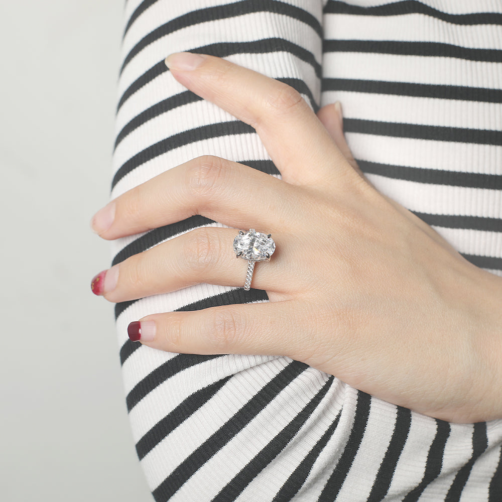 Hand wearing a silver ring with a large gemstone, against a black and white striped background.