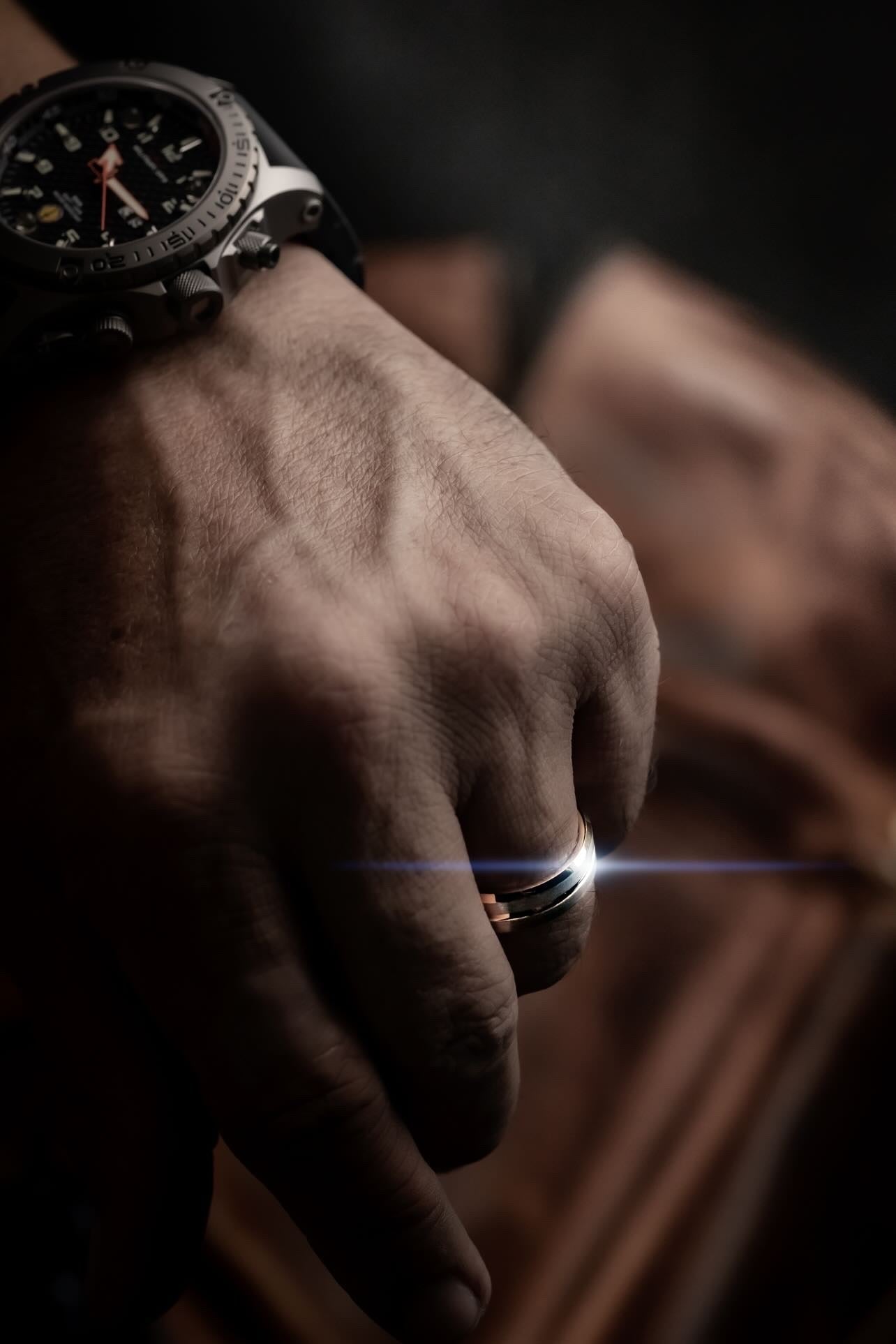 Hand wearing a watch with a close-up of a ring on a dark background