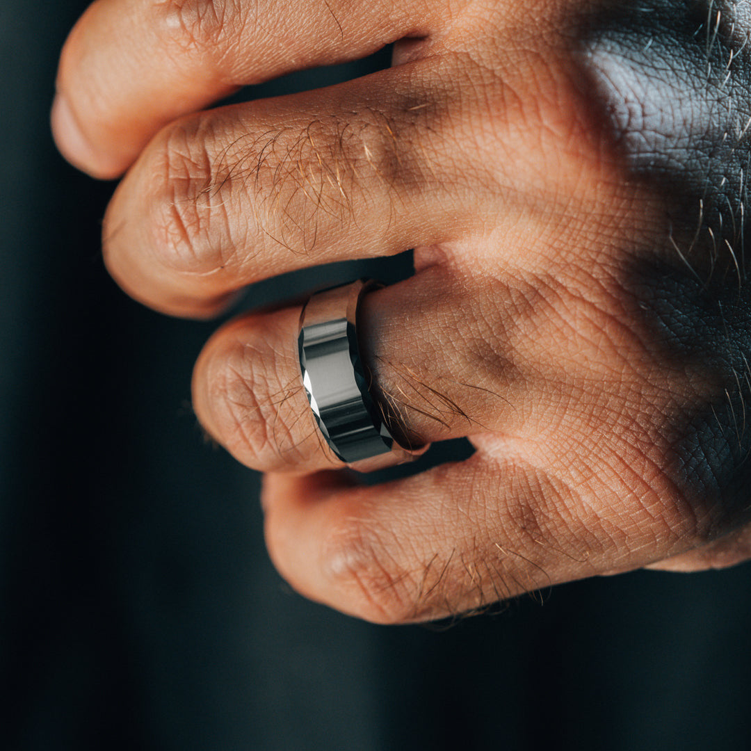 Close-up of a hand wearing a silver ring on a dark background