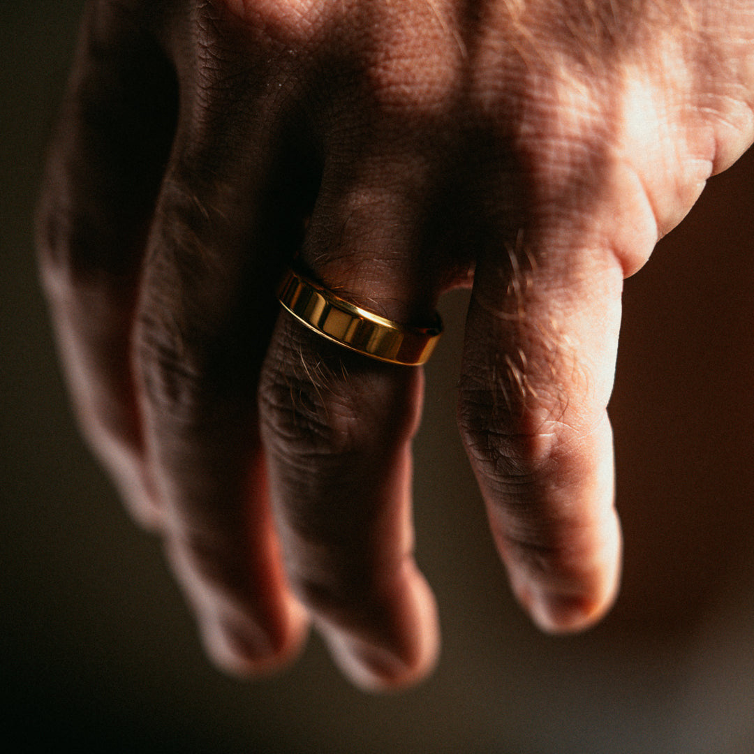Hand wearing a gold ring on a dark background
