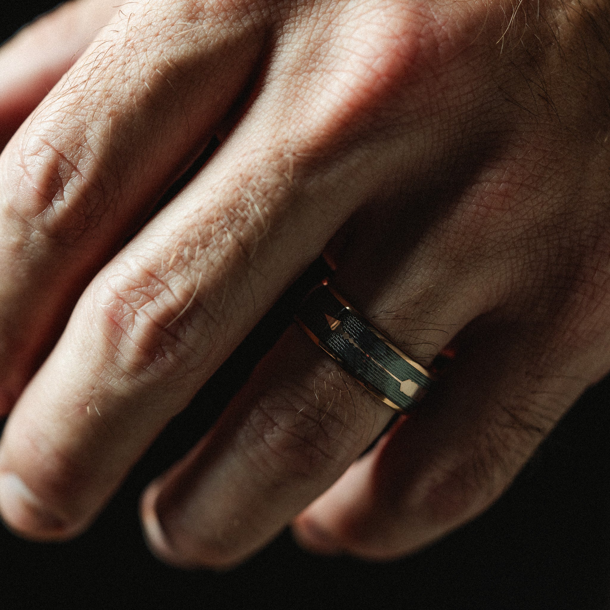 Close-up of a hand wearing a ring with a dark background