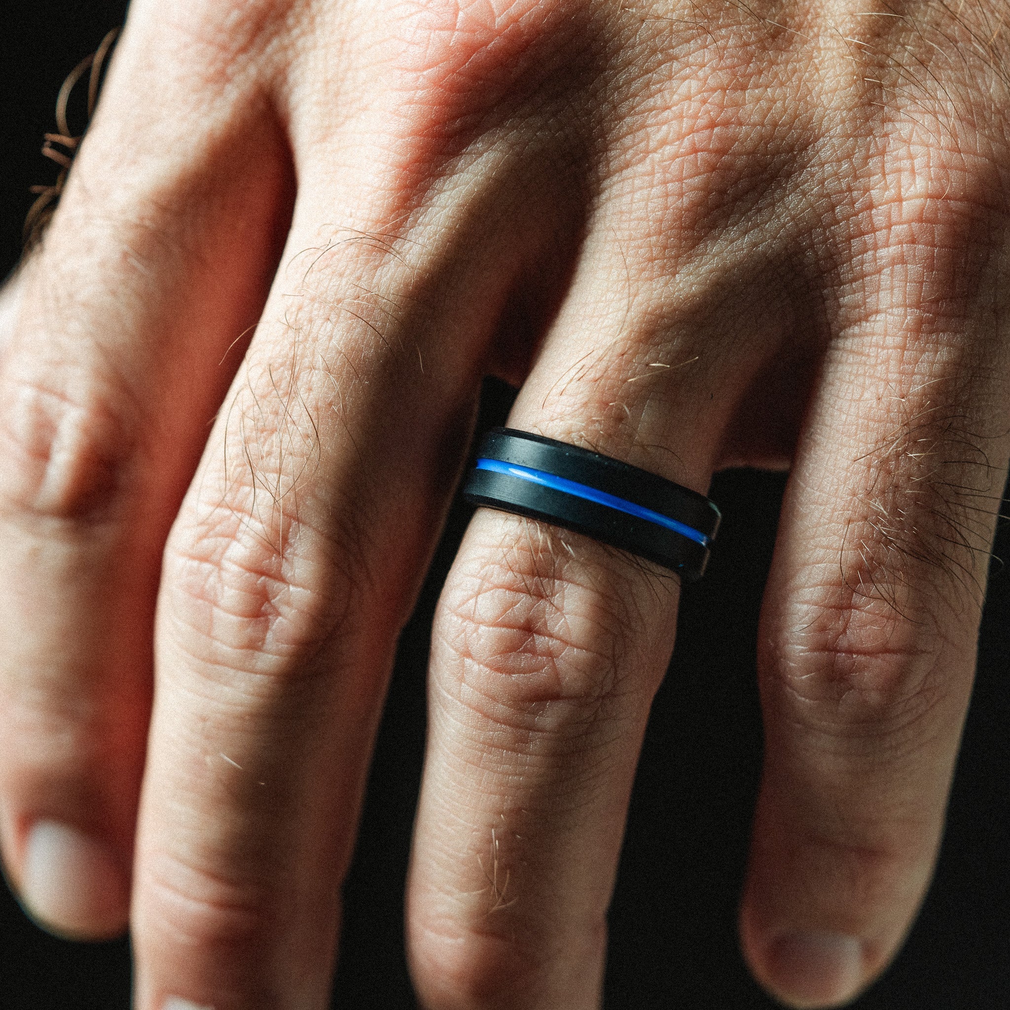 Hand wearing a ring with a blue stripe on a dark background