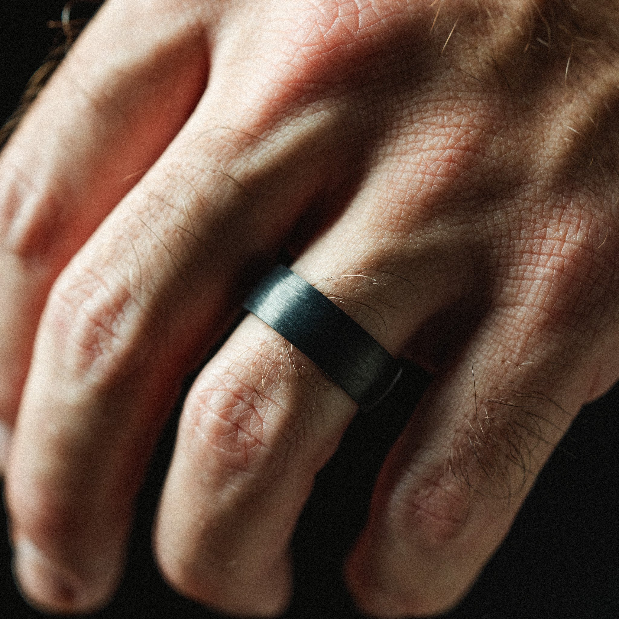 Close-up of a hand wearing a black ring on a dark background