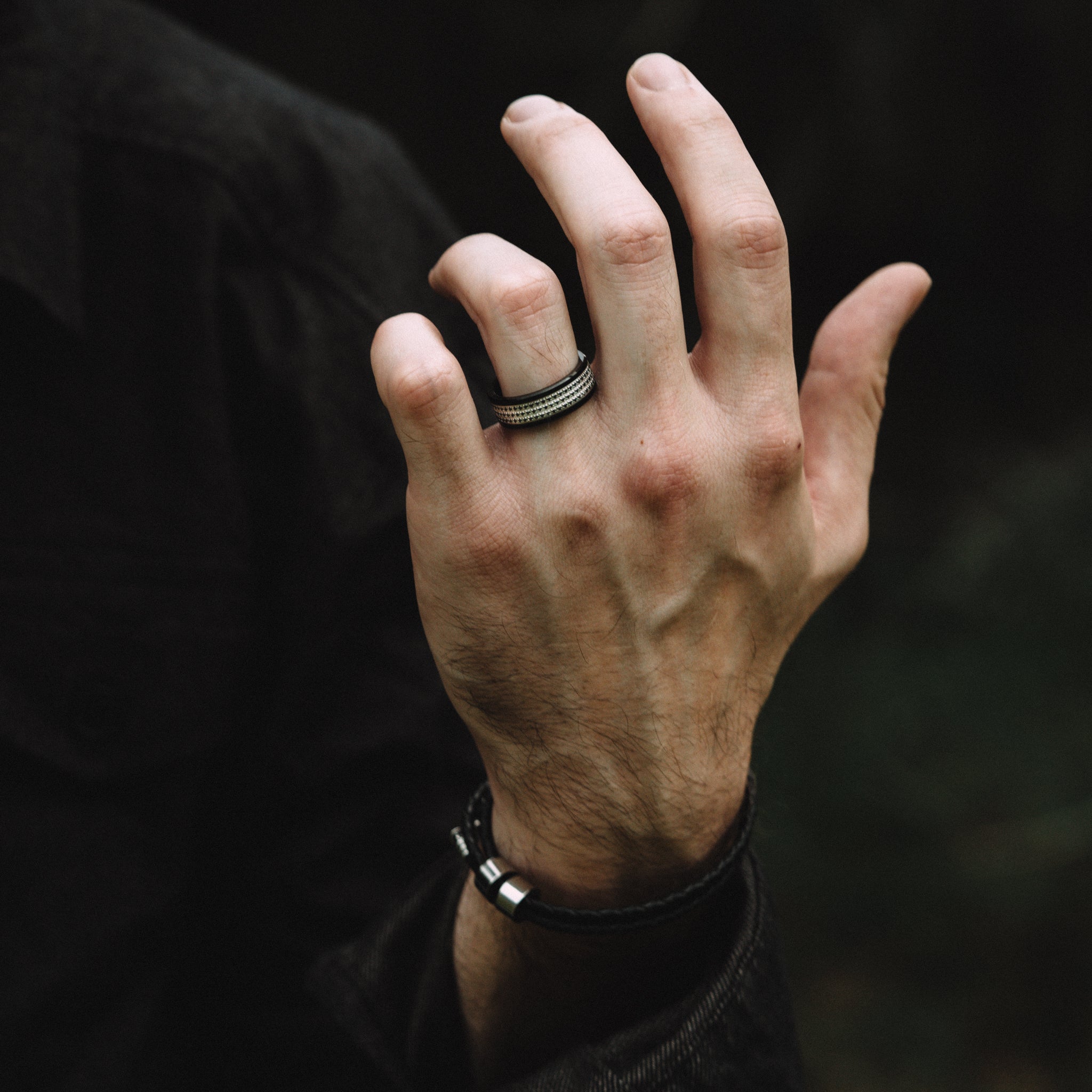Hand wearing a black ring with a dark background