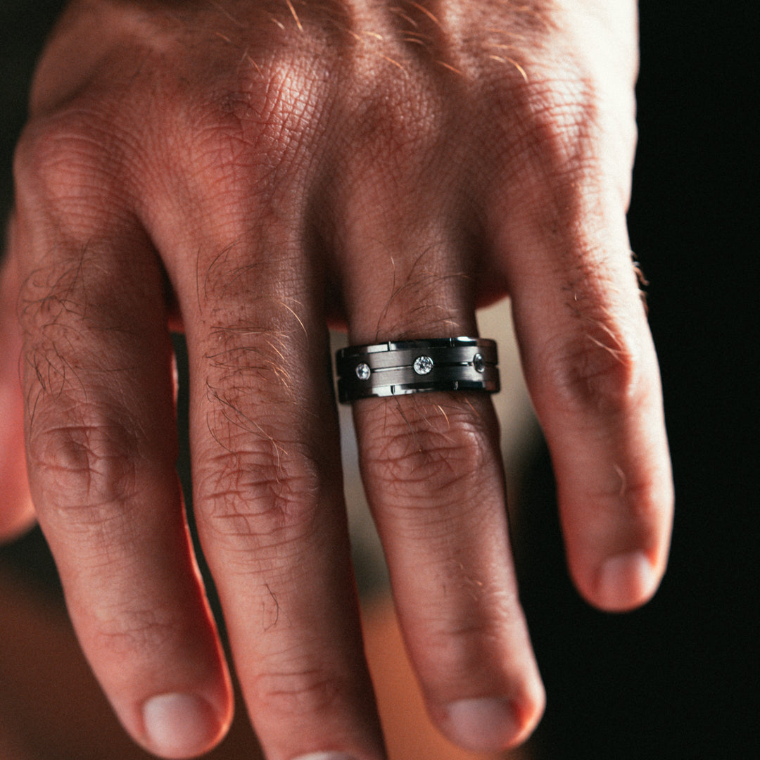 Hand wearing a black ring with a diamond on a dark background