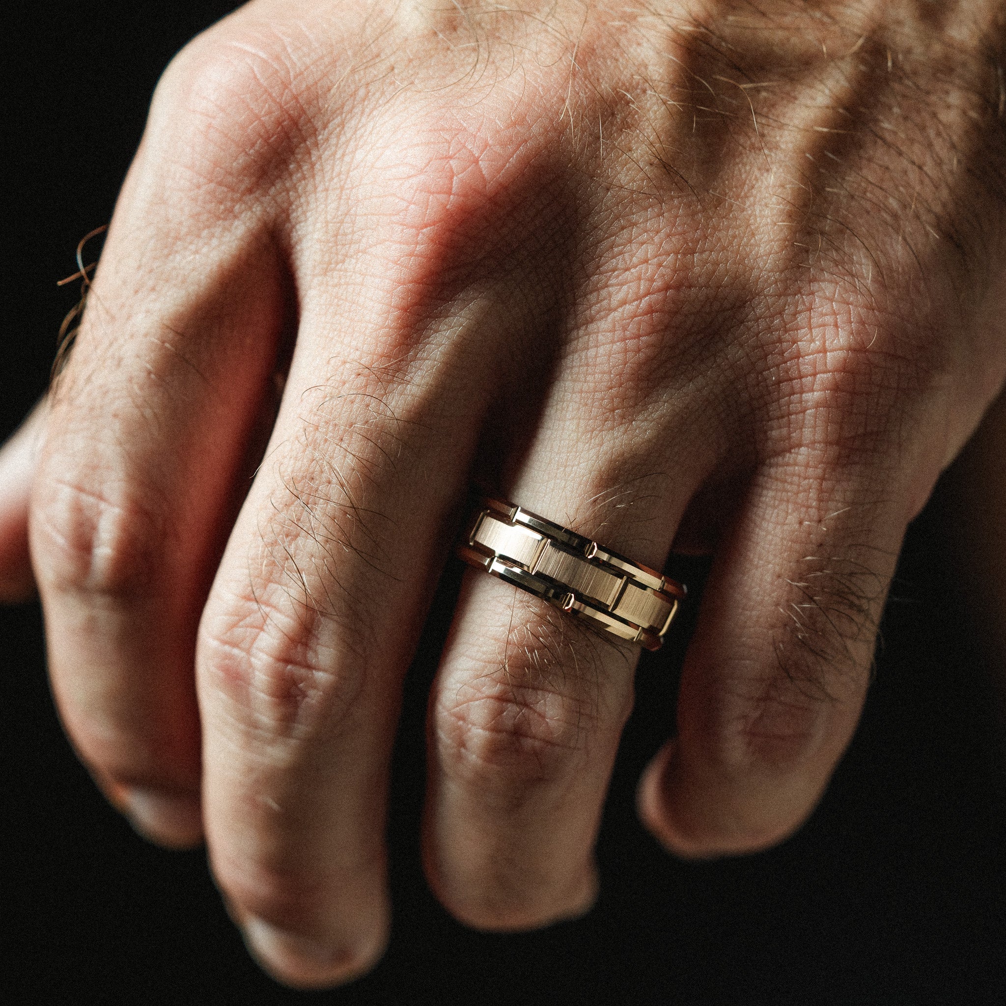 Hand wearing a gold ring on a dark background