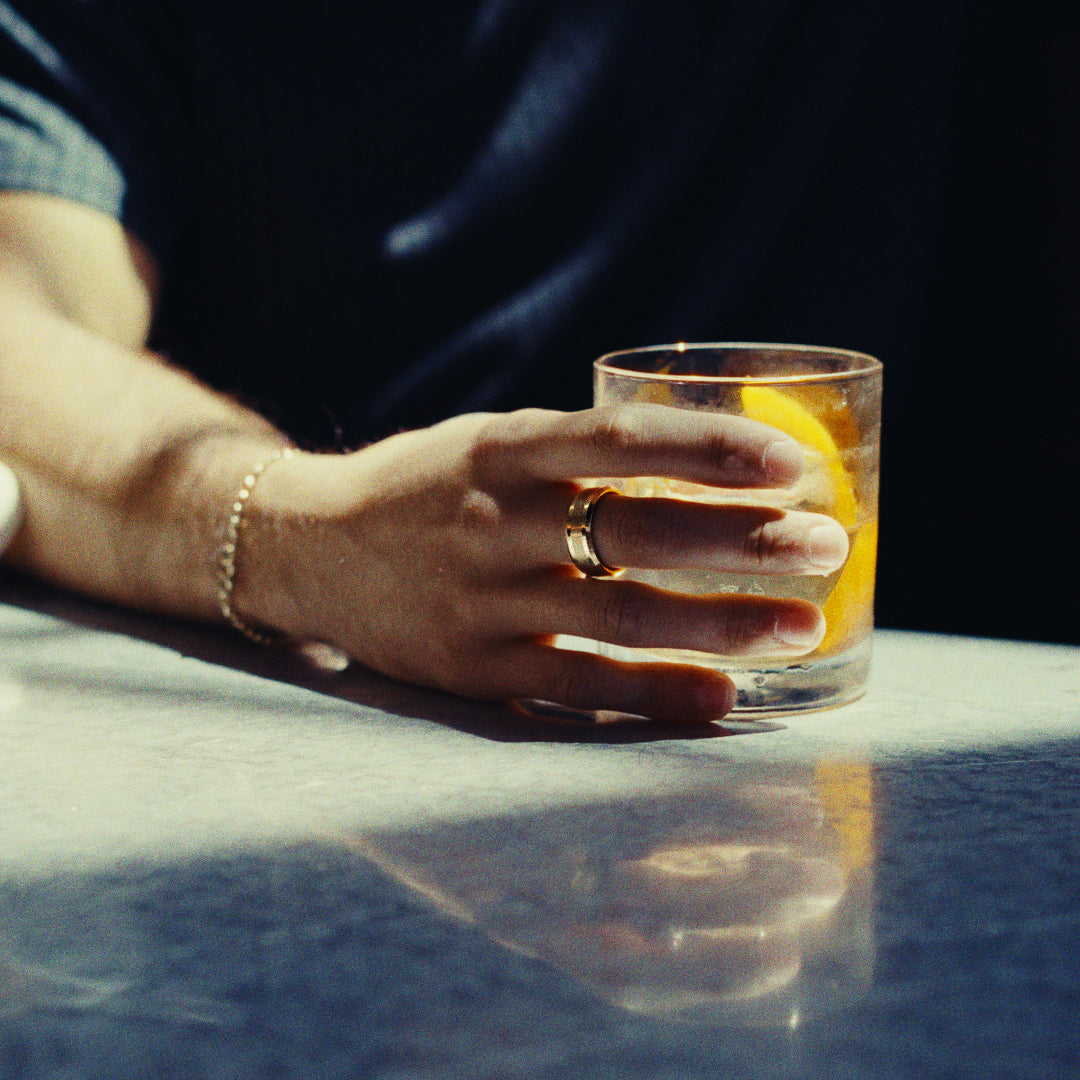 Hand holding a glass with an orange slice on a reflective surface