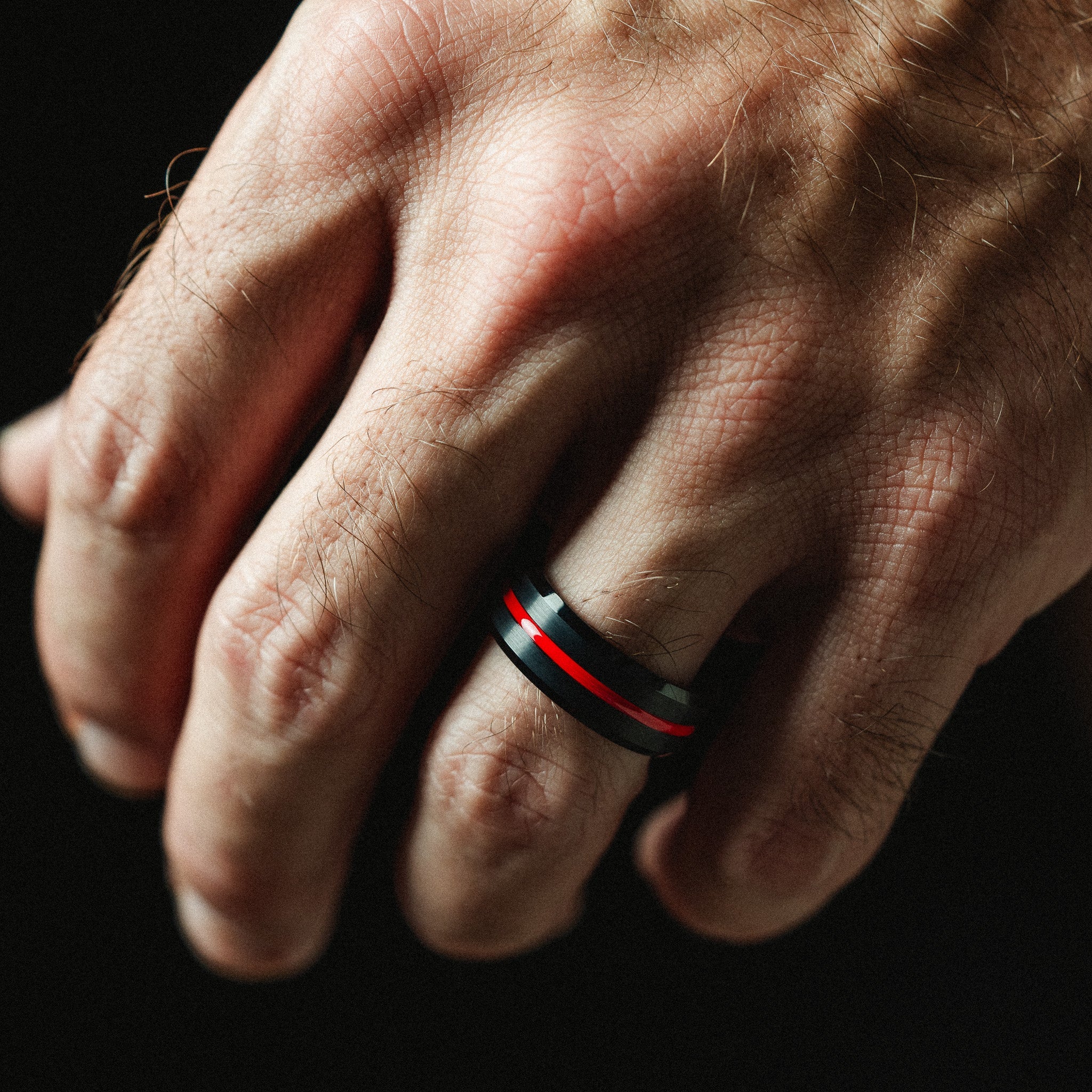 Hand wearing a black ring with red accents on a dark background