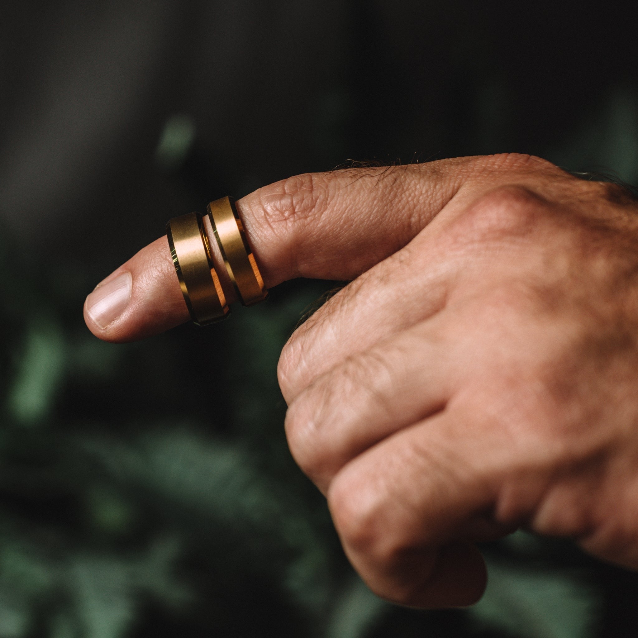 Hand wearing two gold rings on a blurred green background