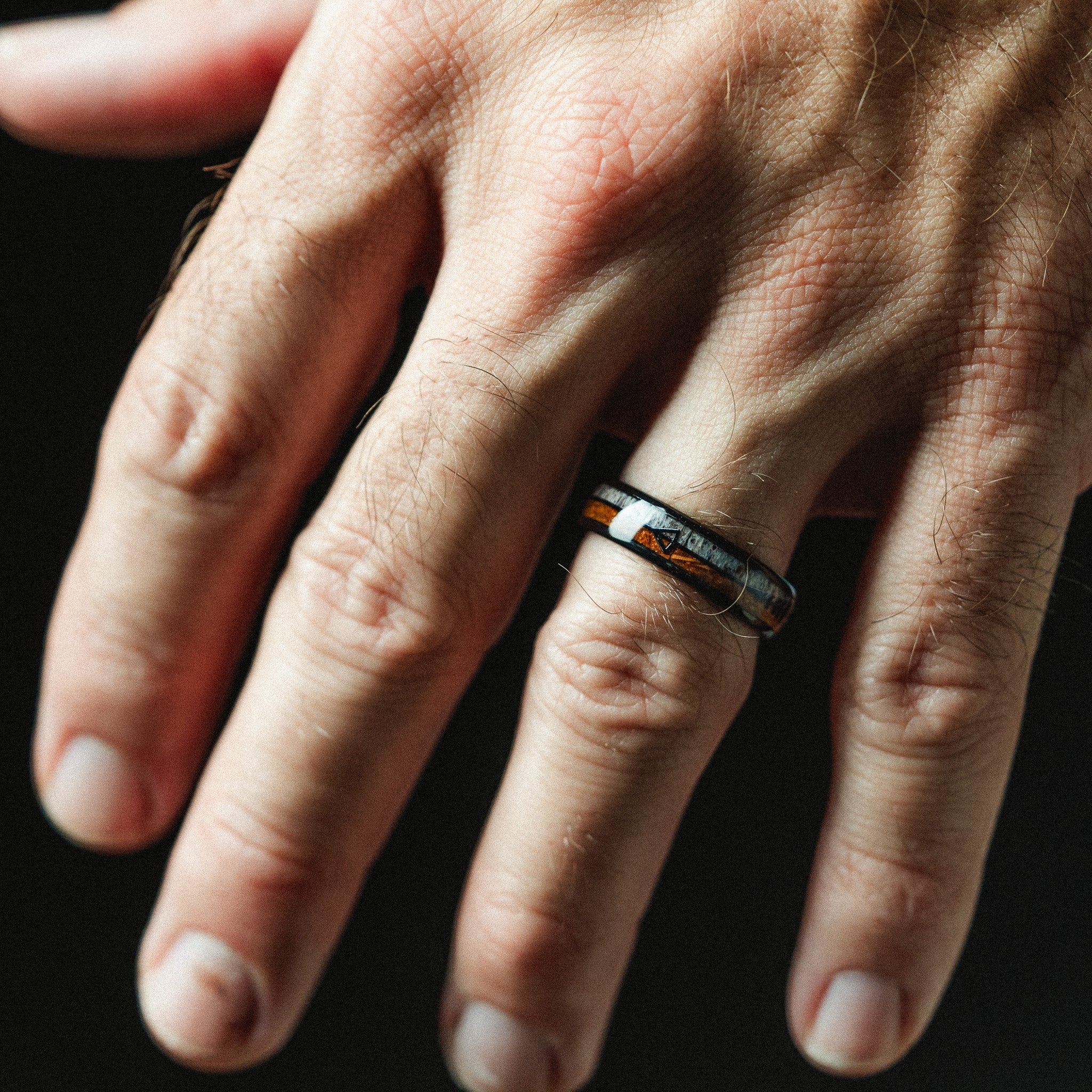 Close-up of a hand wearing a ring with a dark background