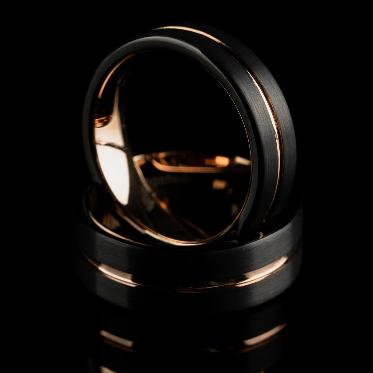 Two black rings with rose gold accents on a reflective black surface