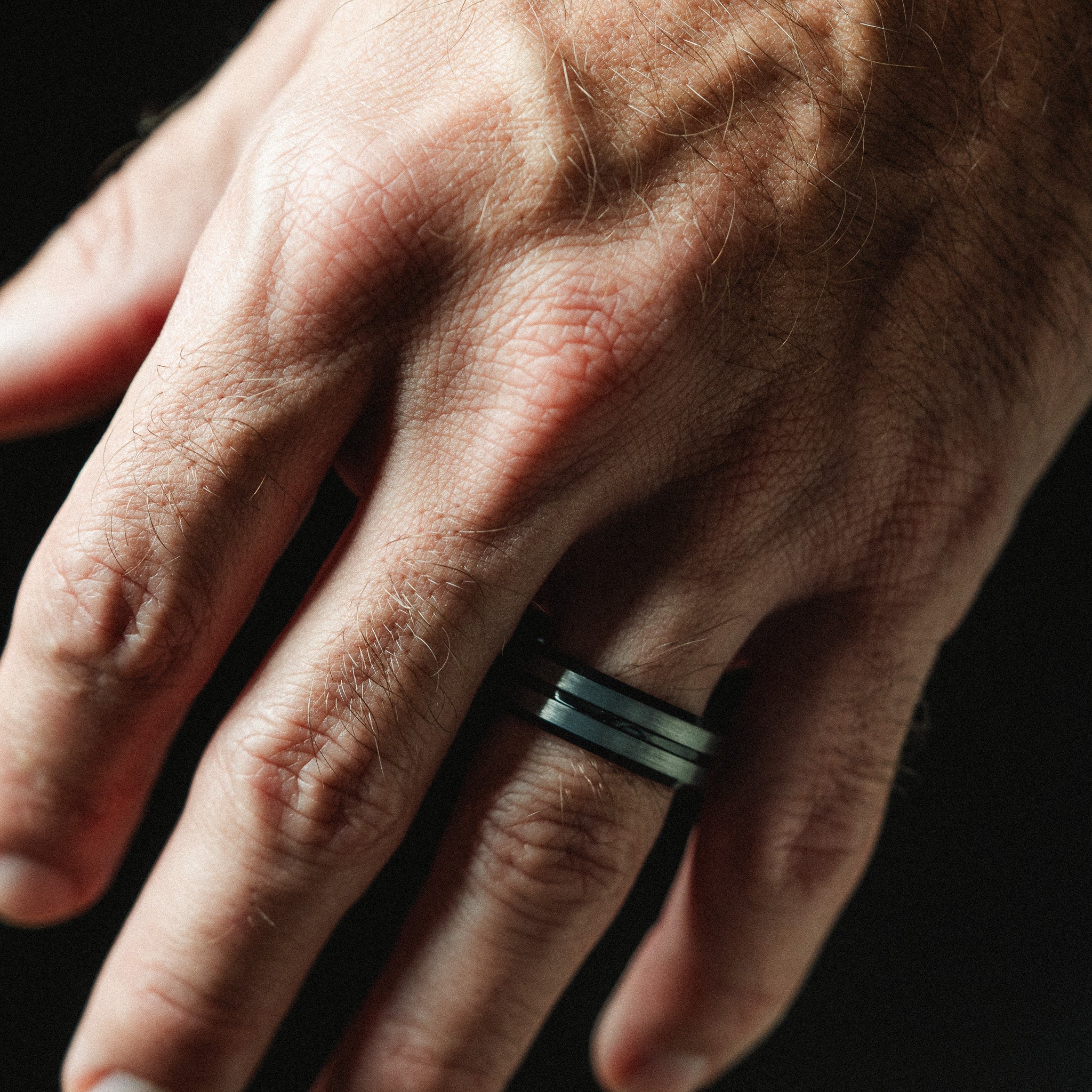 Close-up of a hand wearing a black and green ring on a dark background