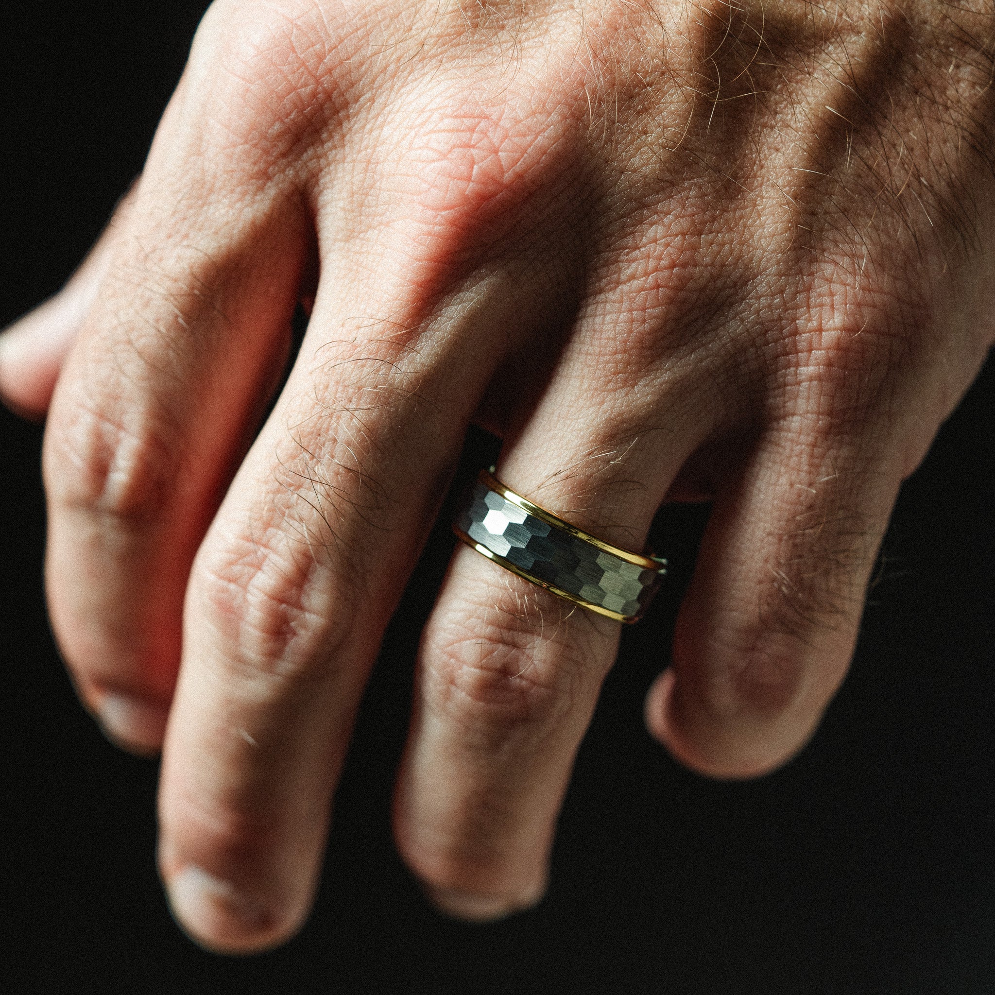 Hand wearing a gold and black ring on a dark background