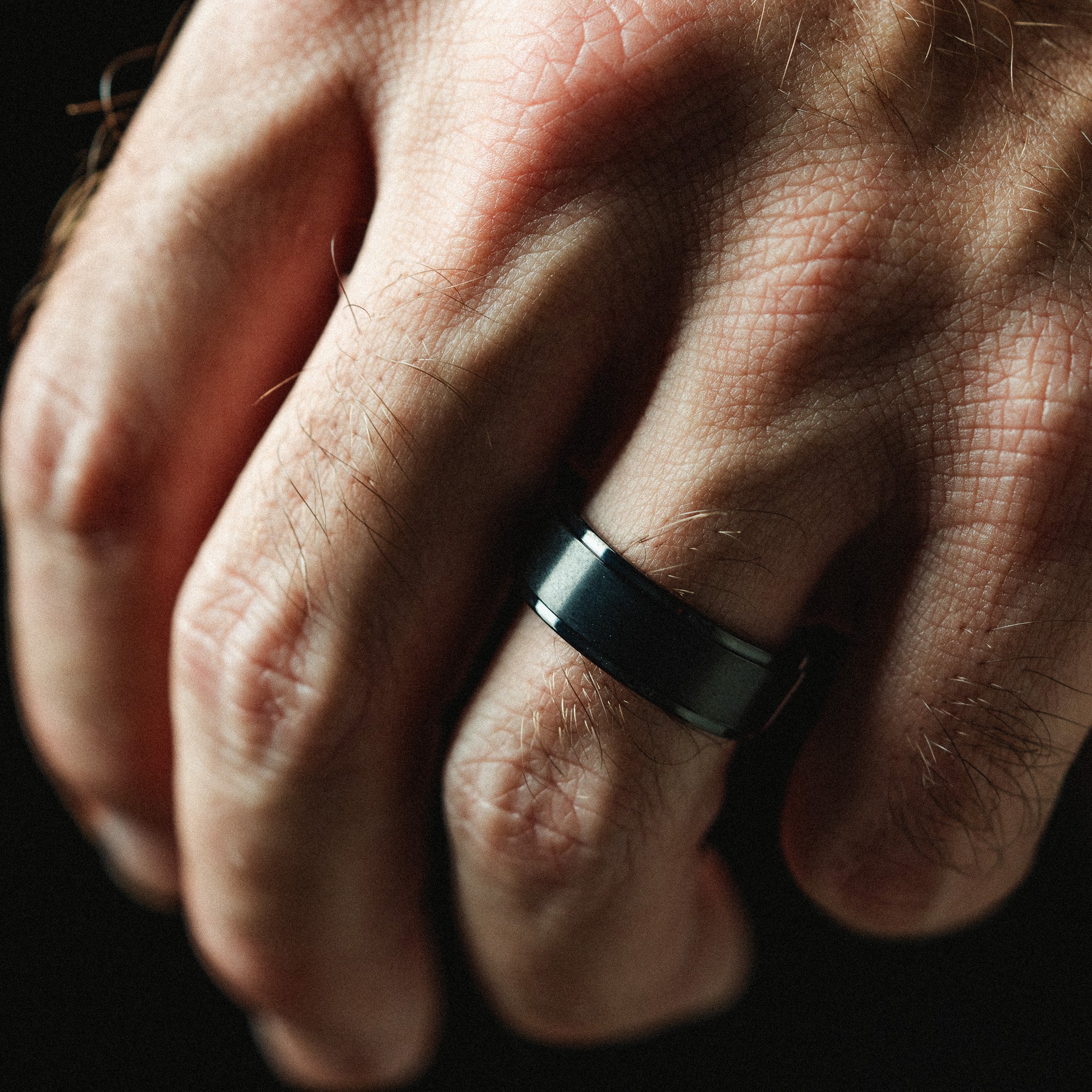 Close-up of a hand wearing a black ring on a dark background