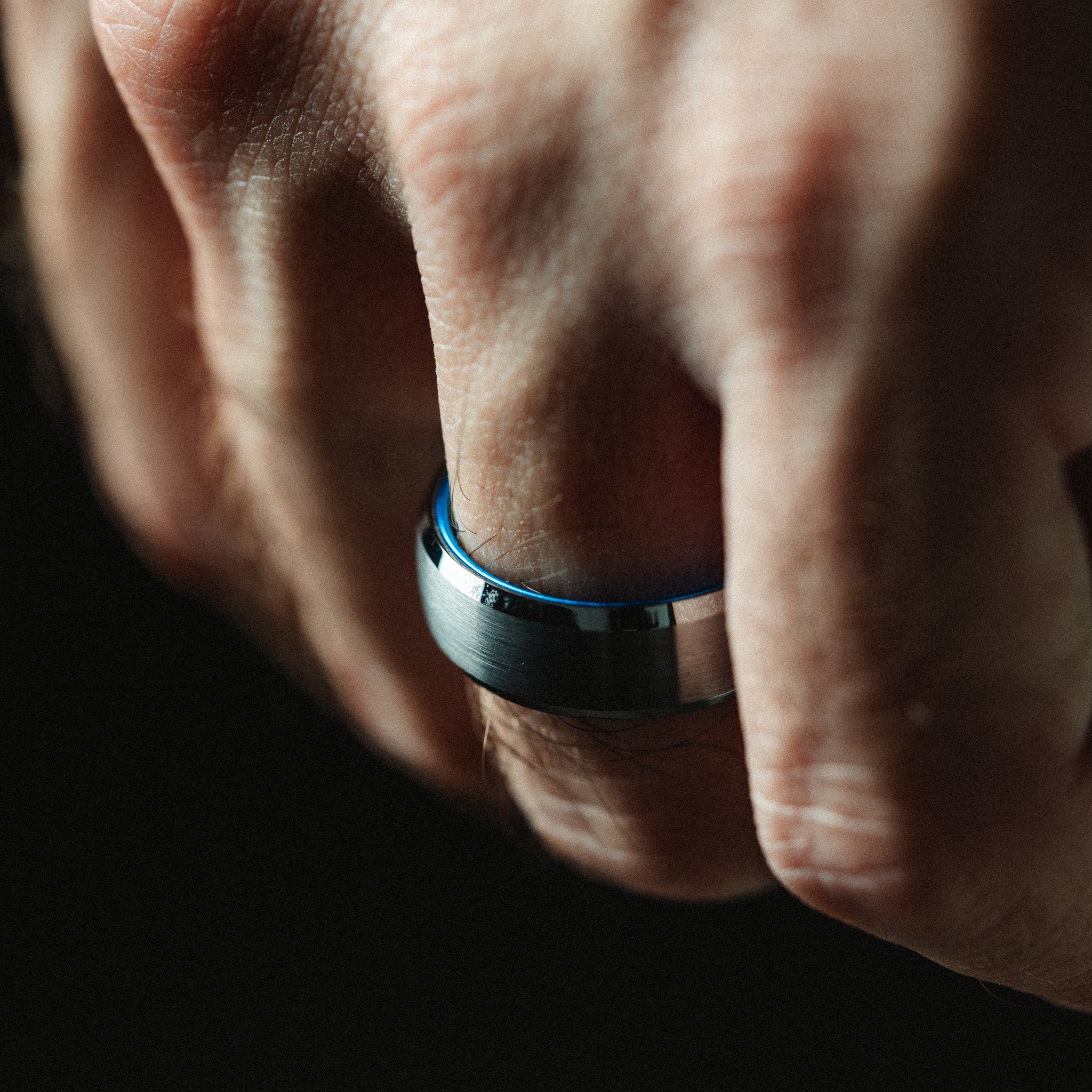 Close-up of a hand wearing a blue and black ring on a dark background