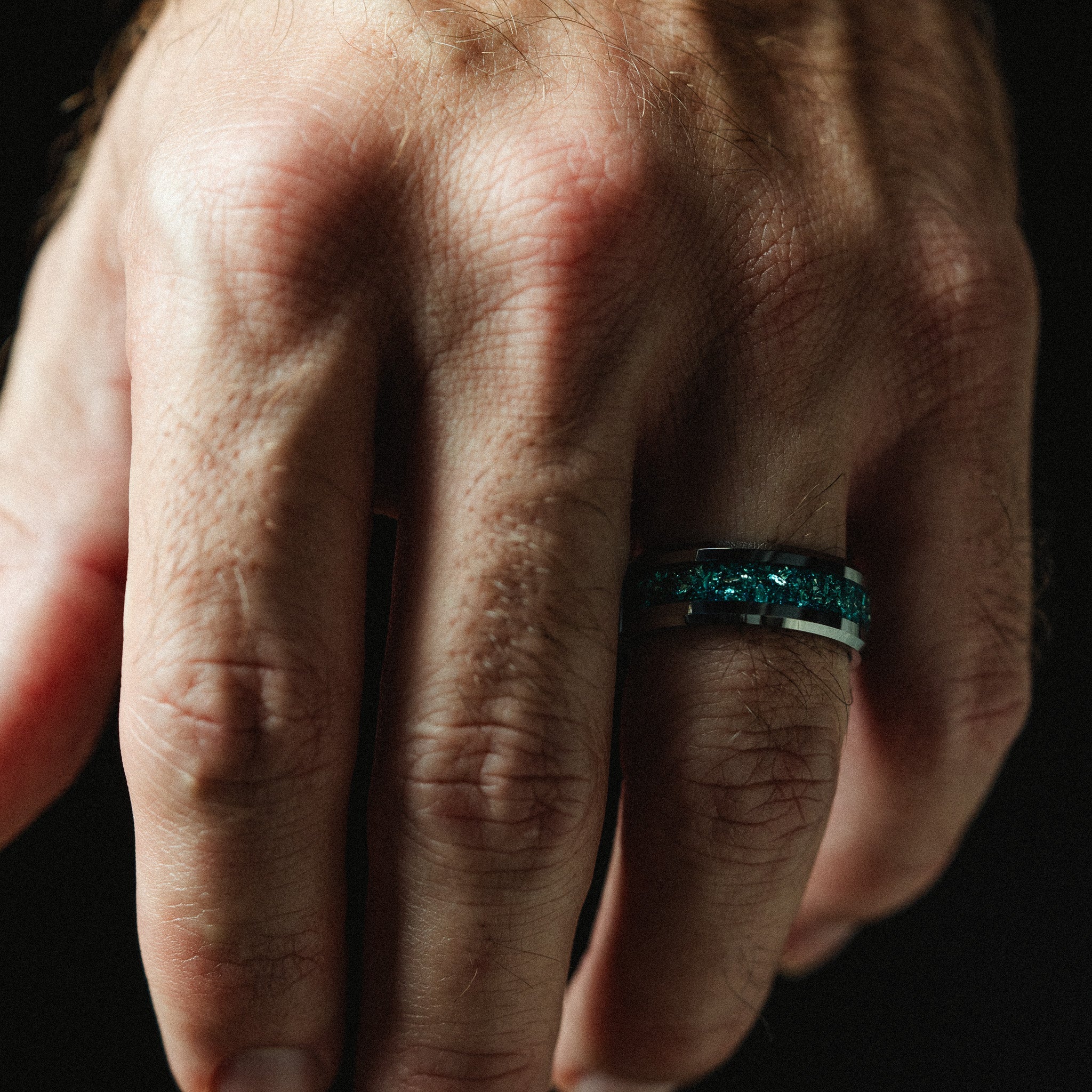 Close-up of a hand wearing a green ring on a dark background