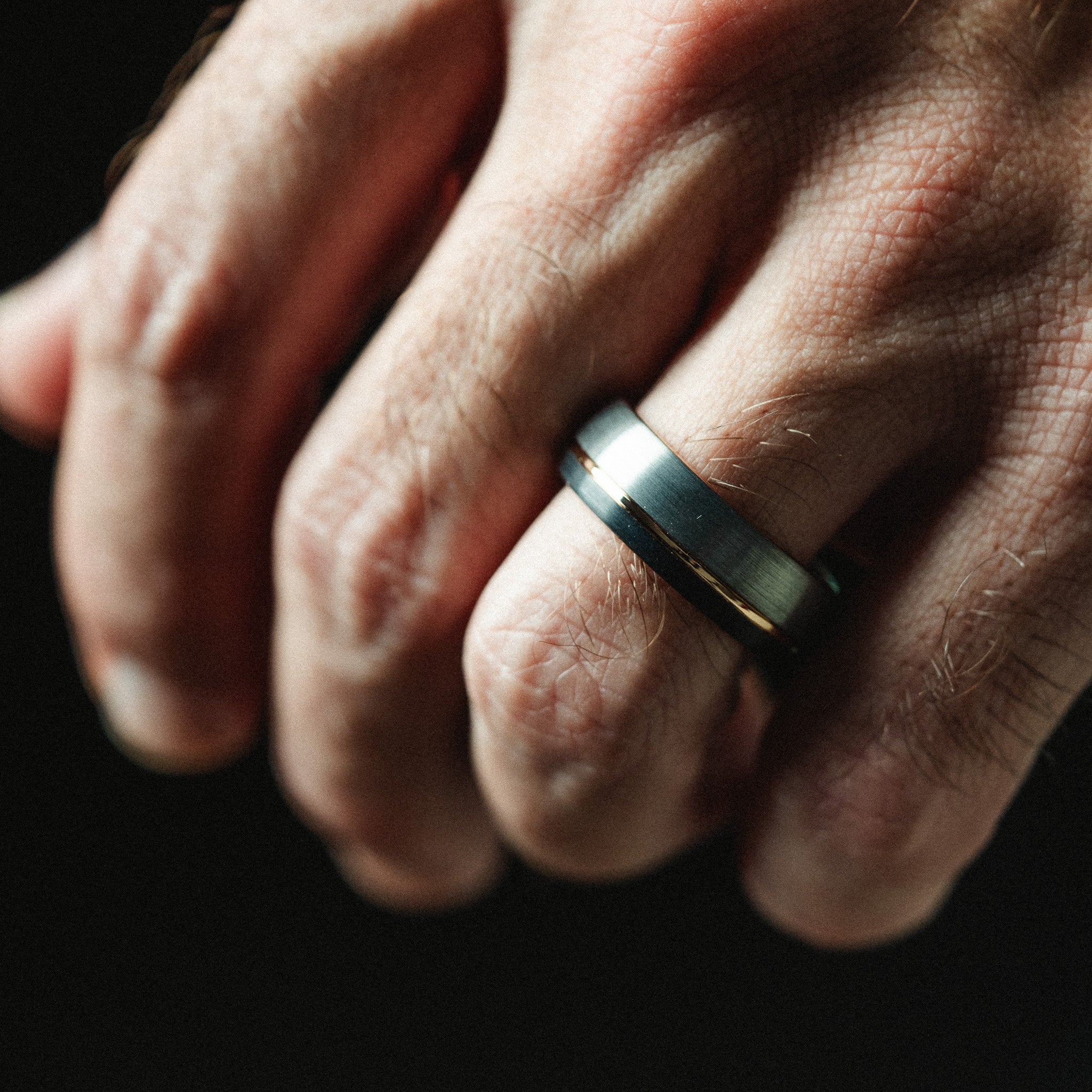 Close-up of a hand wearing a ring on a dark background